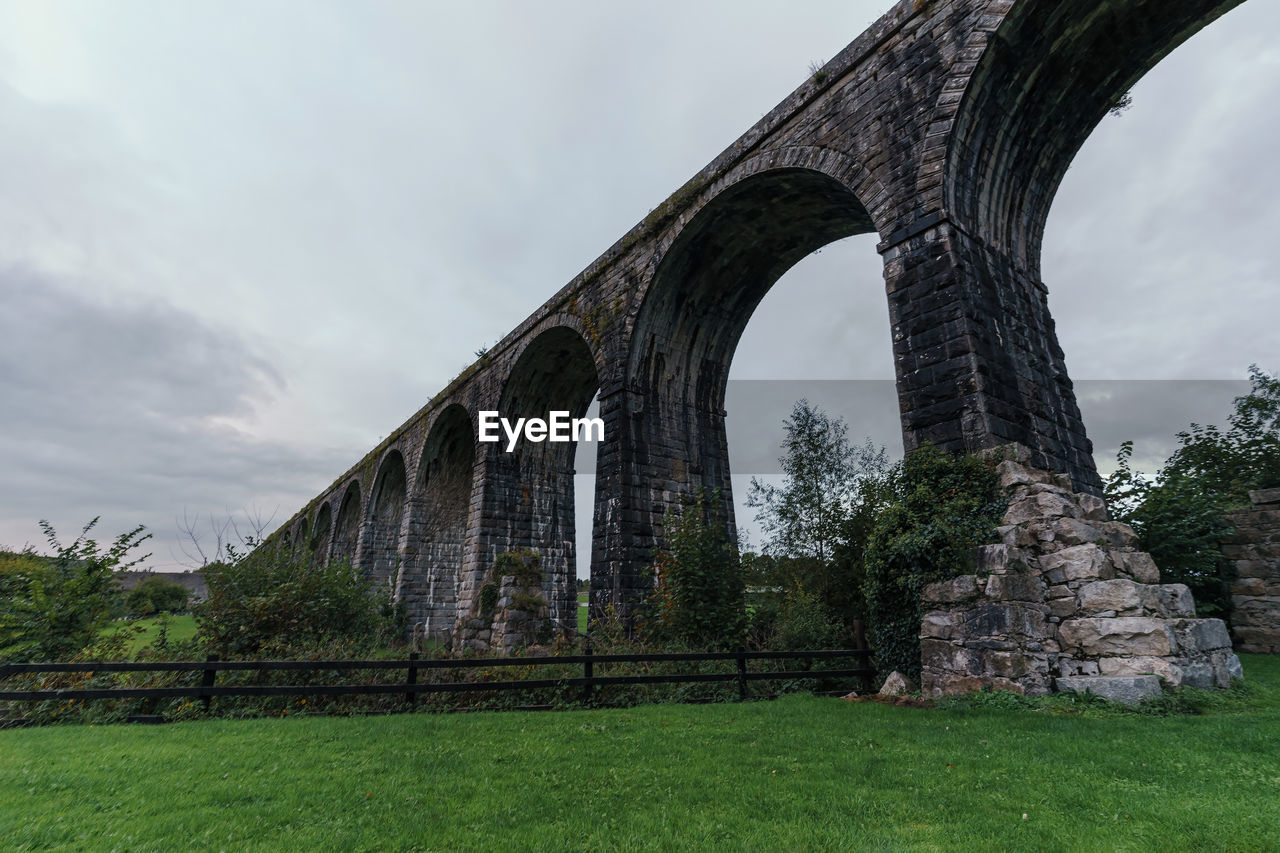 architecture, built structure, bridge, landmark, sky, plant, arch, cloud, nature, grass, travel destinations, history, viaduct, the past, no people, tree, aqueduct, ruins, outdoors, travel, environment, day, landscape, low angle view, tourism, green, arch bridge