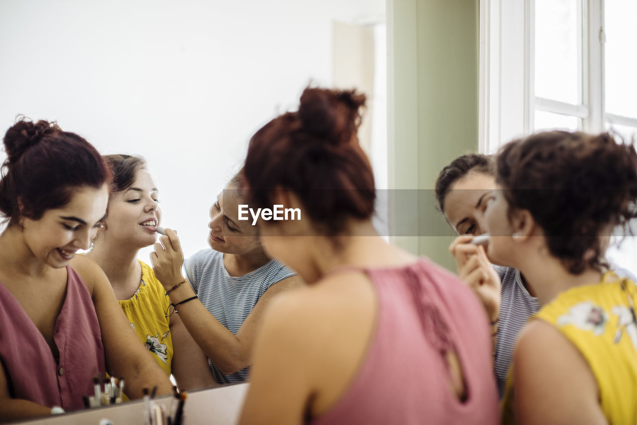 Cheerful diverse women doing makeup together at home