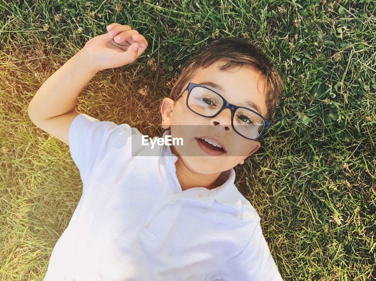 Directly above portrait of boy in eyeglasses lying on grassy field at public park