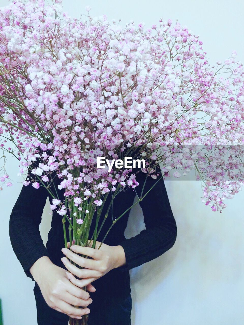 Person holding pink flowers against wall