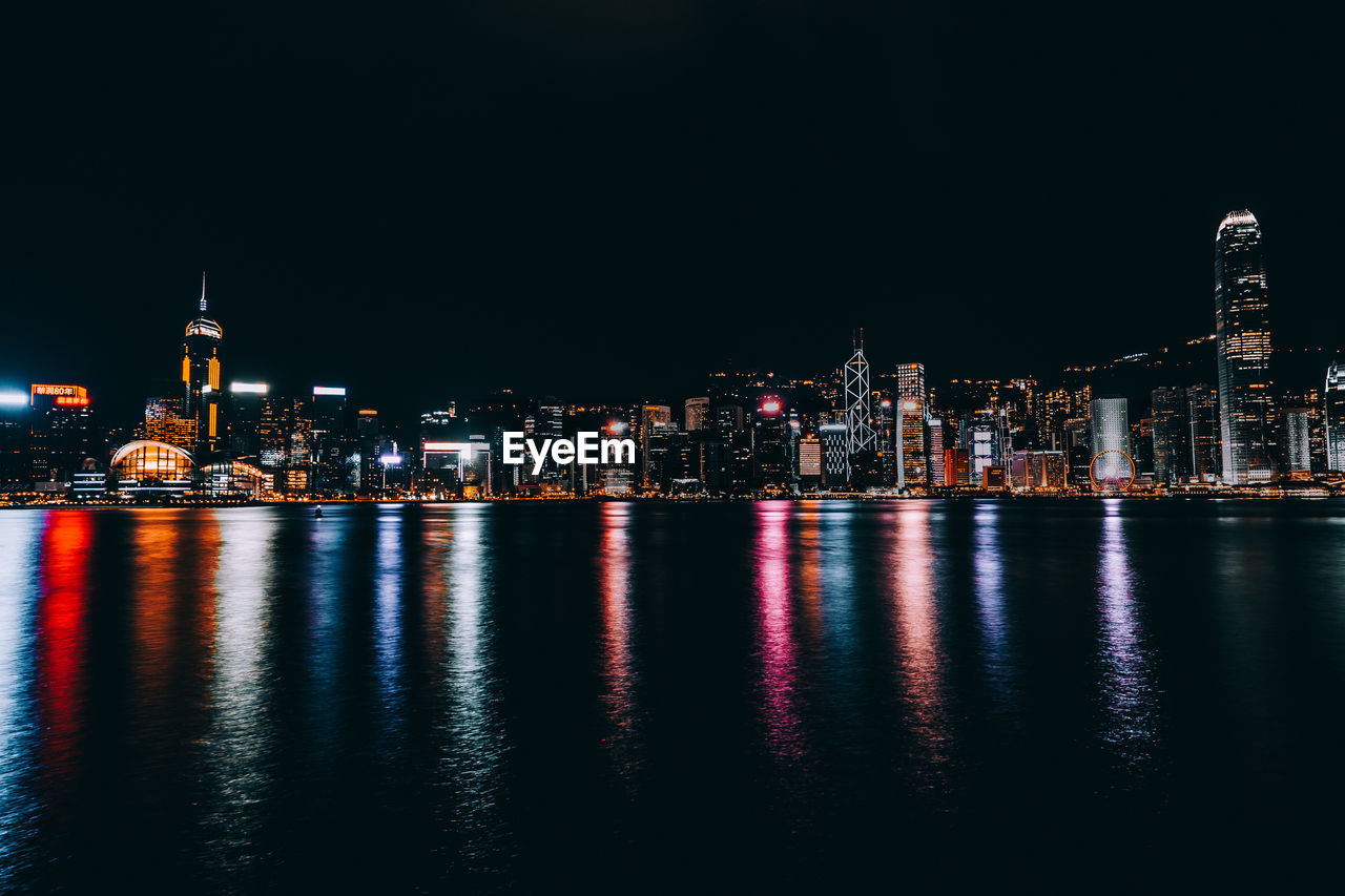 Illuminated buildings by river against sky at night