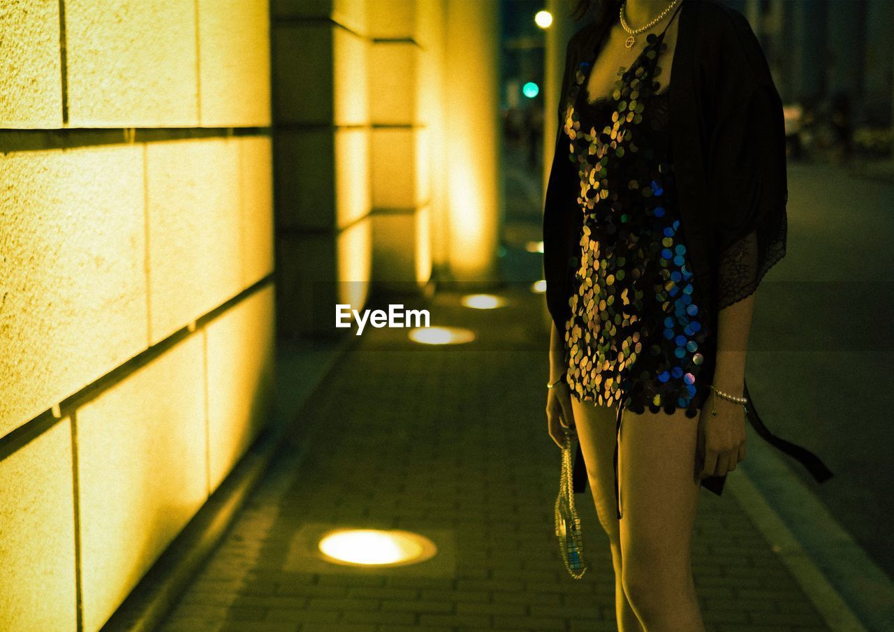 Midsection of woman standing on illuminated sidewalk at night
