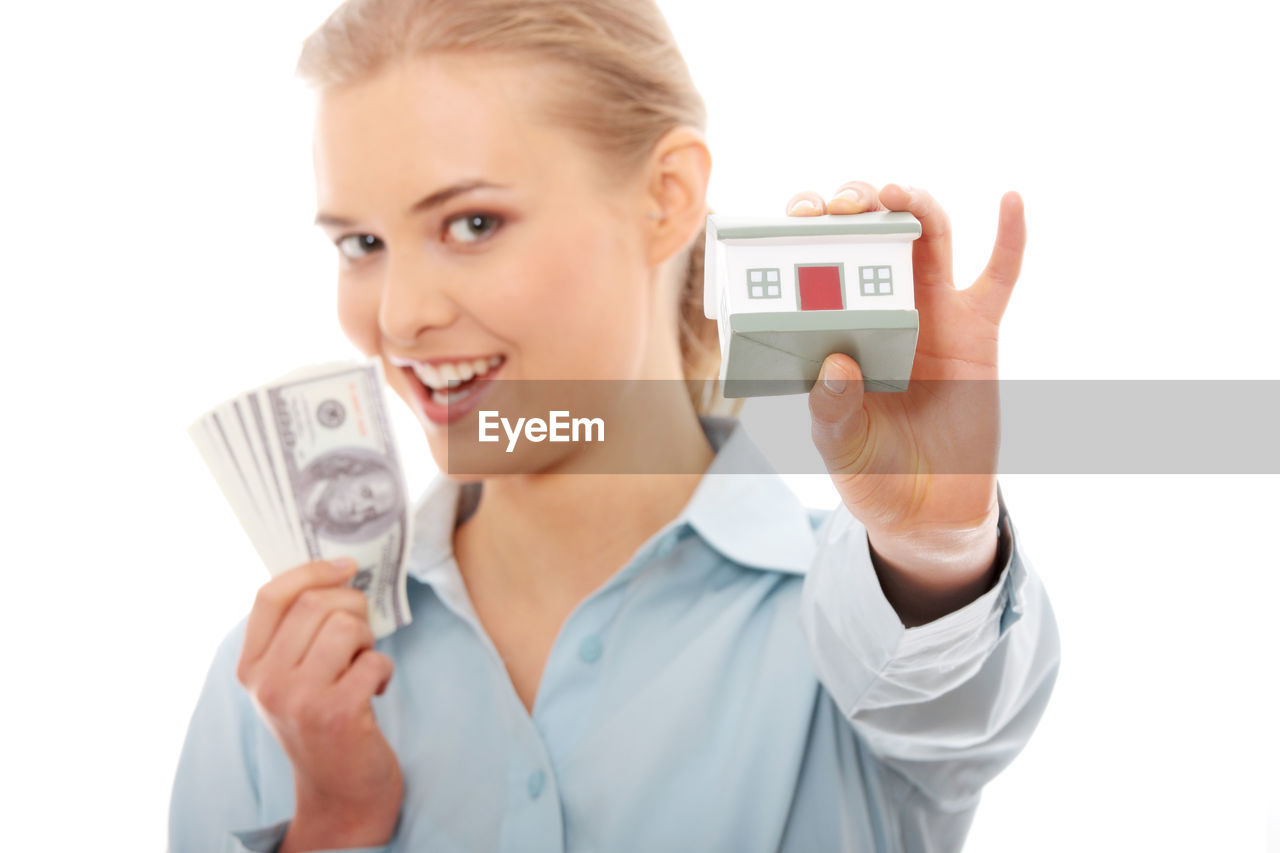 Portrait of real estate agent with papery currency and model home standing against white background