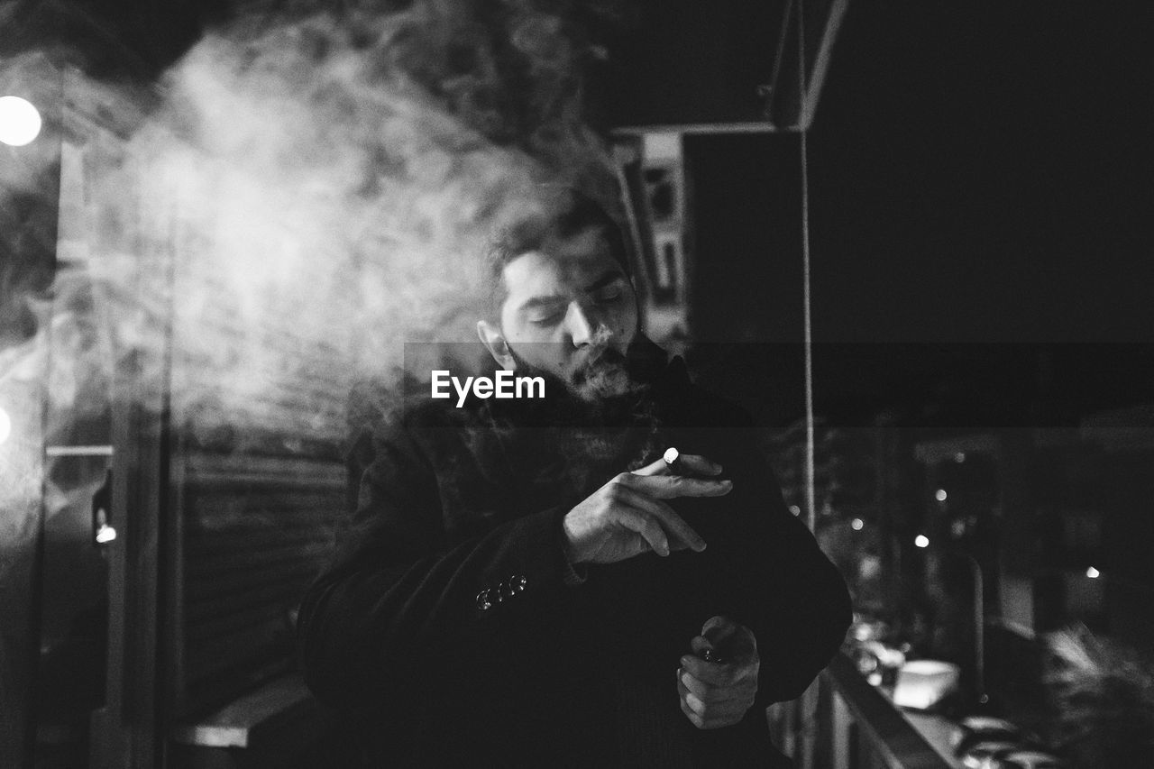 Young man smoking cigarette in darkroom