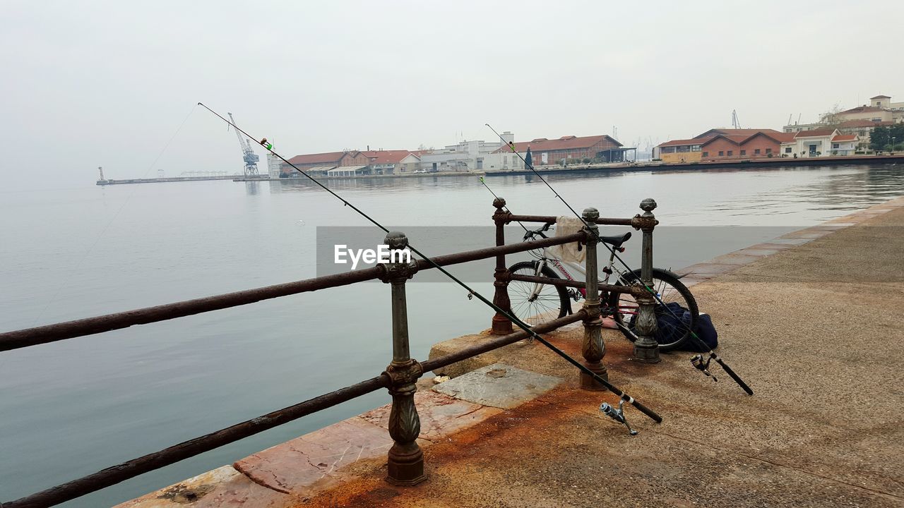 Fishing rods and bicycle leaning on railing at pier in sea against sky