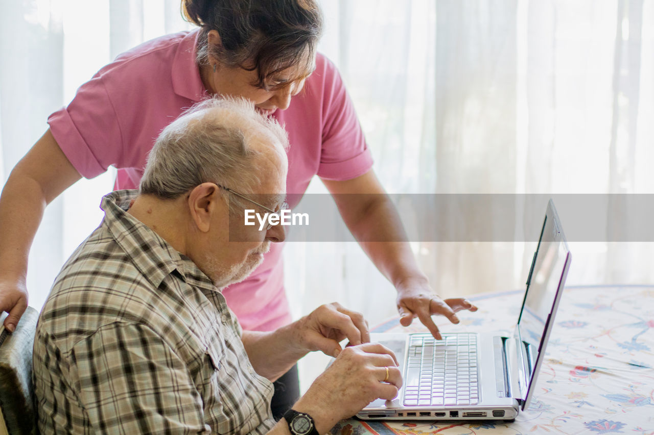 Nurse assisting senior man in typing