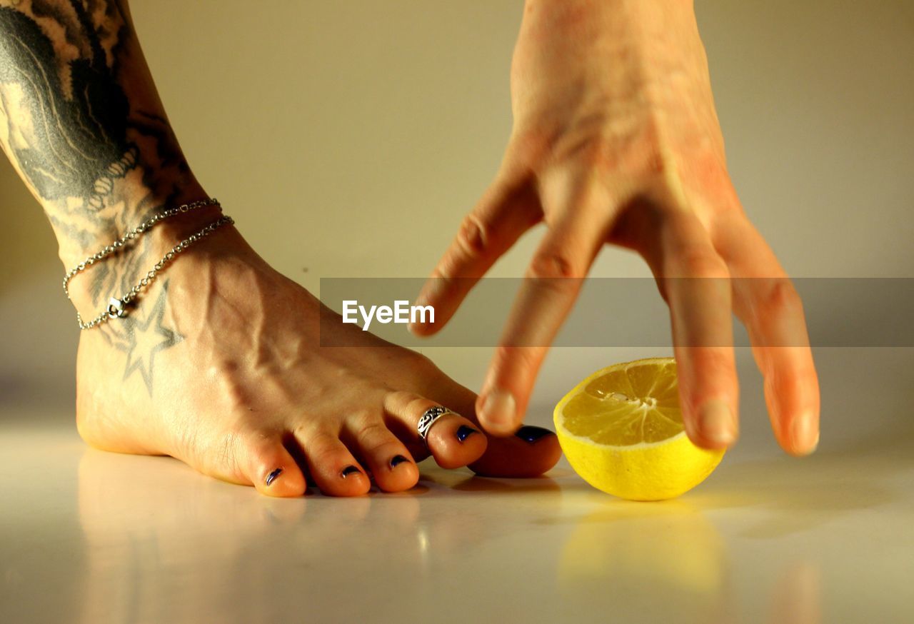 Low section of woman's bare foot and hand with lemon