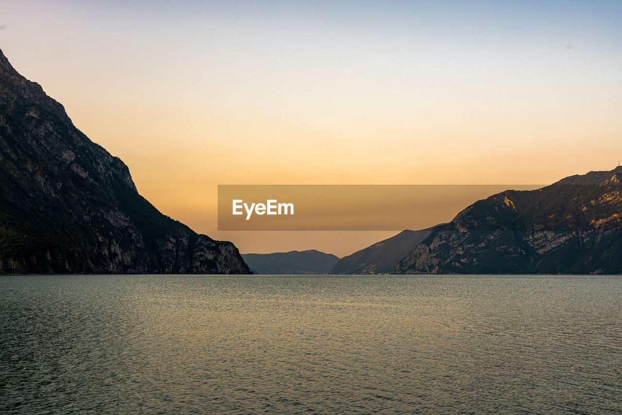 Scenic view of sea by mountains against sky during sunset