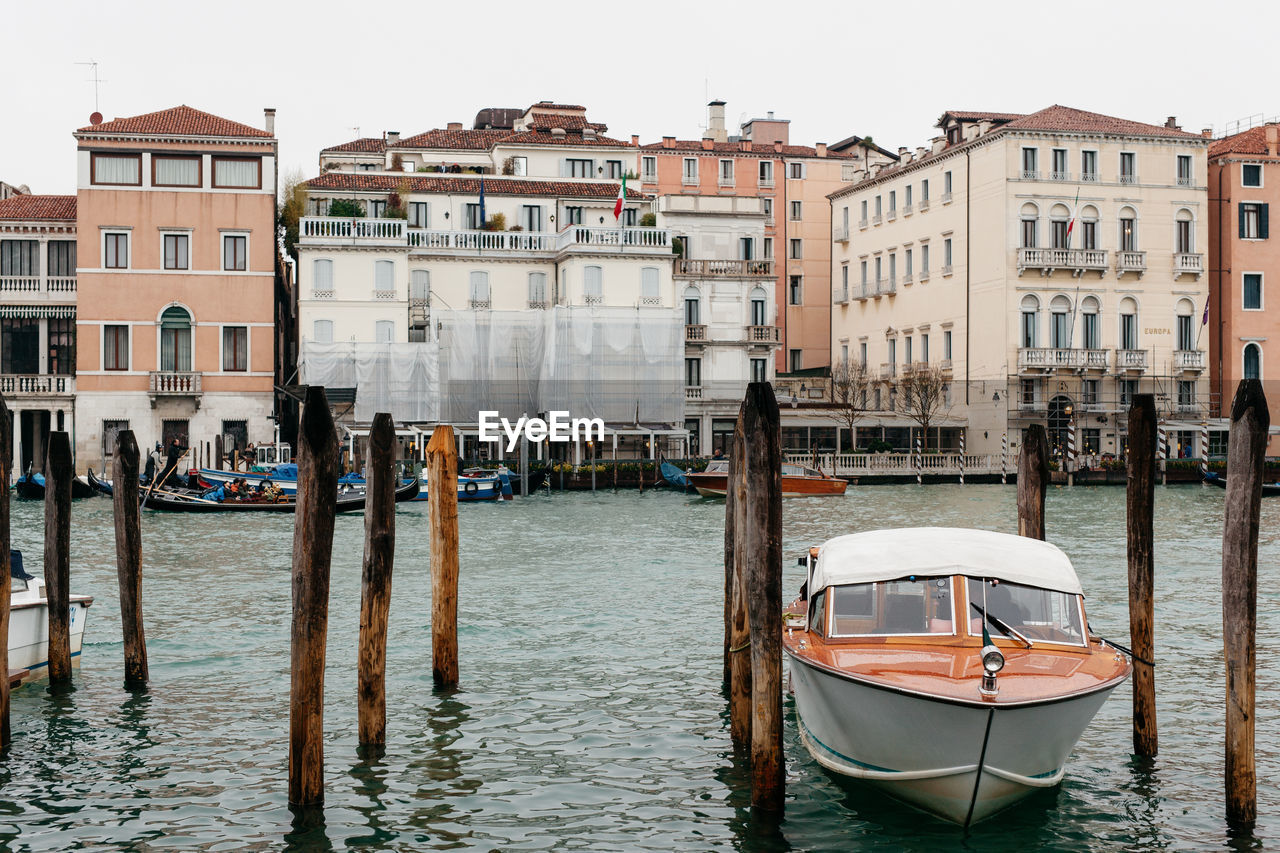 Boat moored amidst wooden posts in canal against buildings