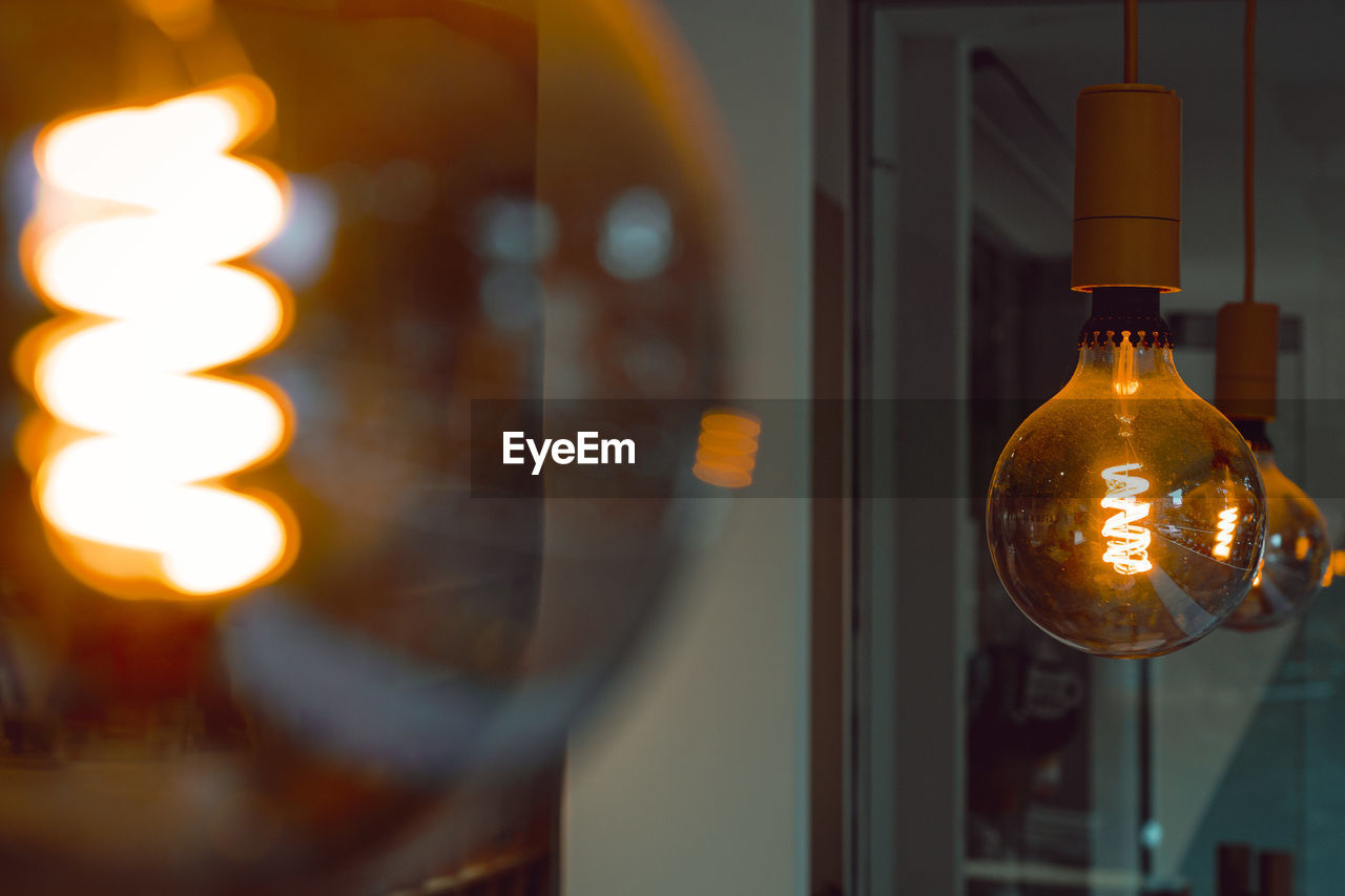 CLOSE-UP OF ILLUMINATED LIGHT BULBS HANGING FROM WINDOW