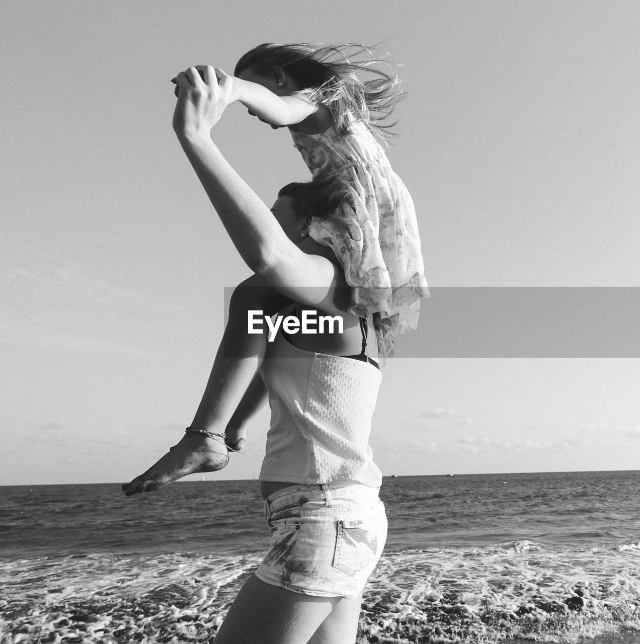 Side view of woman carrying daughter on shoulder at beach