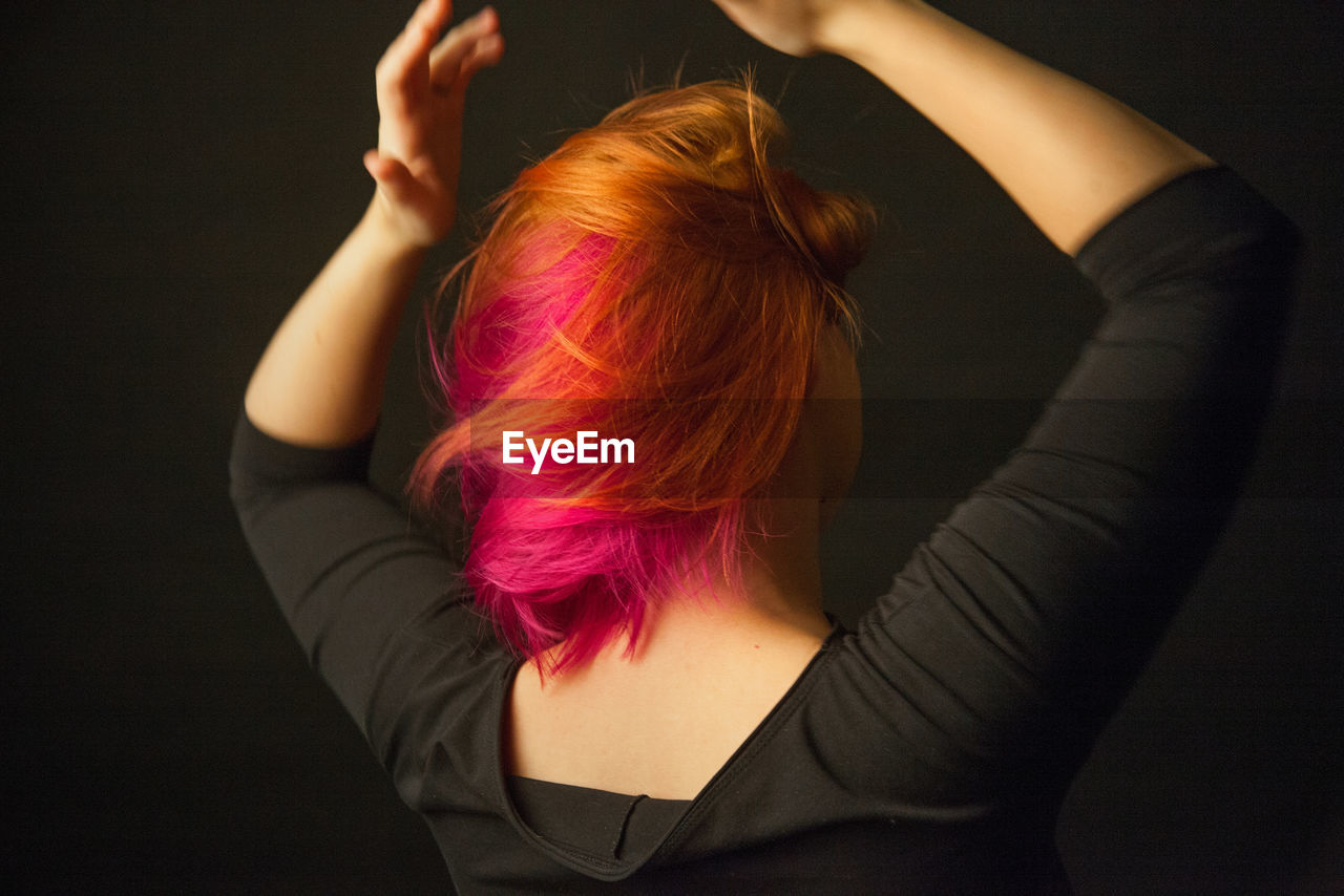 Rear view of woman dancing against black background with colorful hair