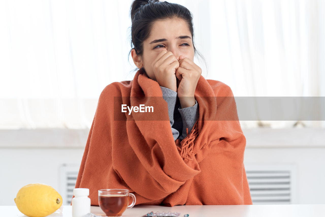 Sick woman wearing blanket sitting at home