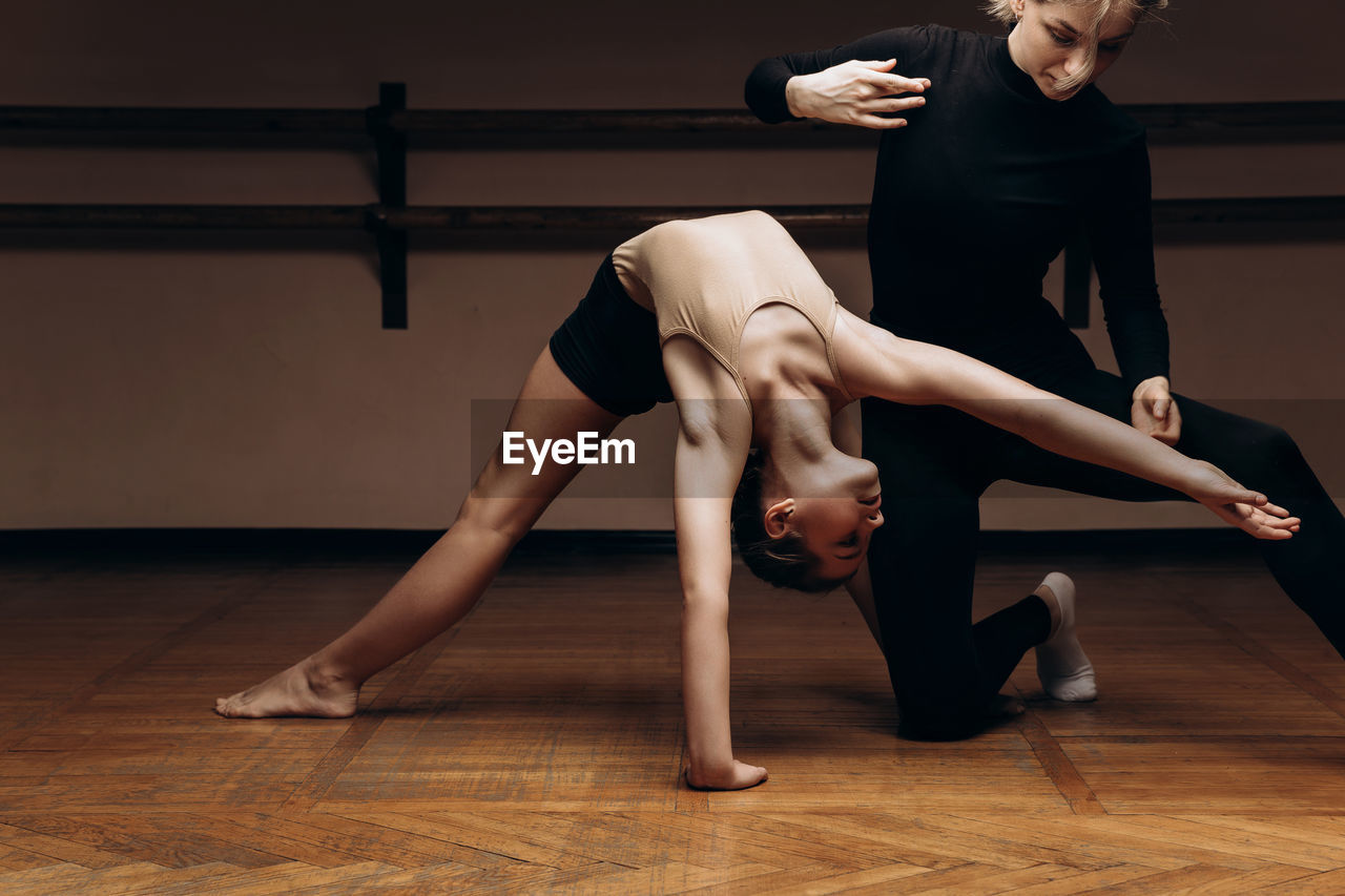 Portrait of a choreographer's teacher helping a little girl to pose correctlyin a dance studio