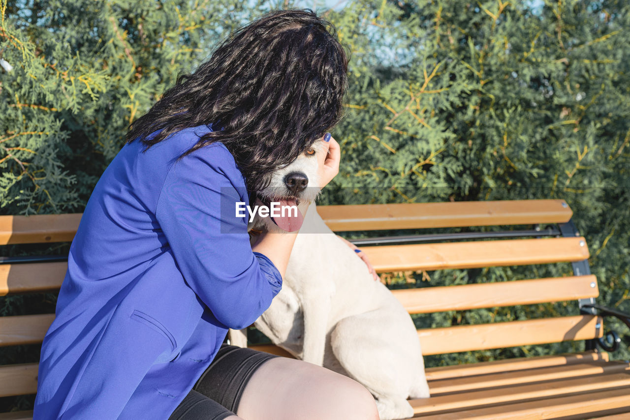 Side view of woman sitting on bench hugging her dog