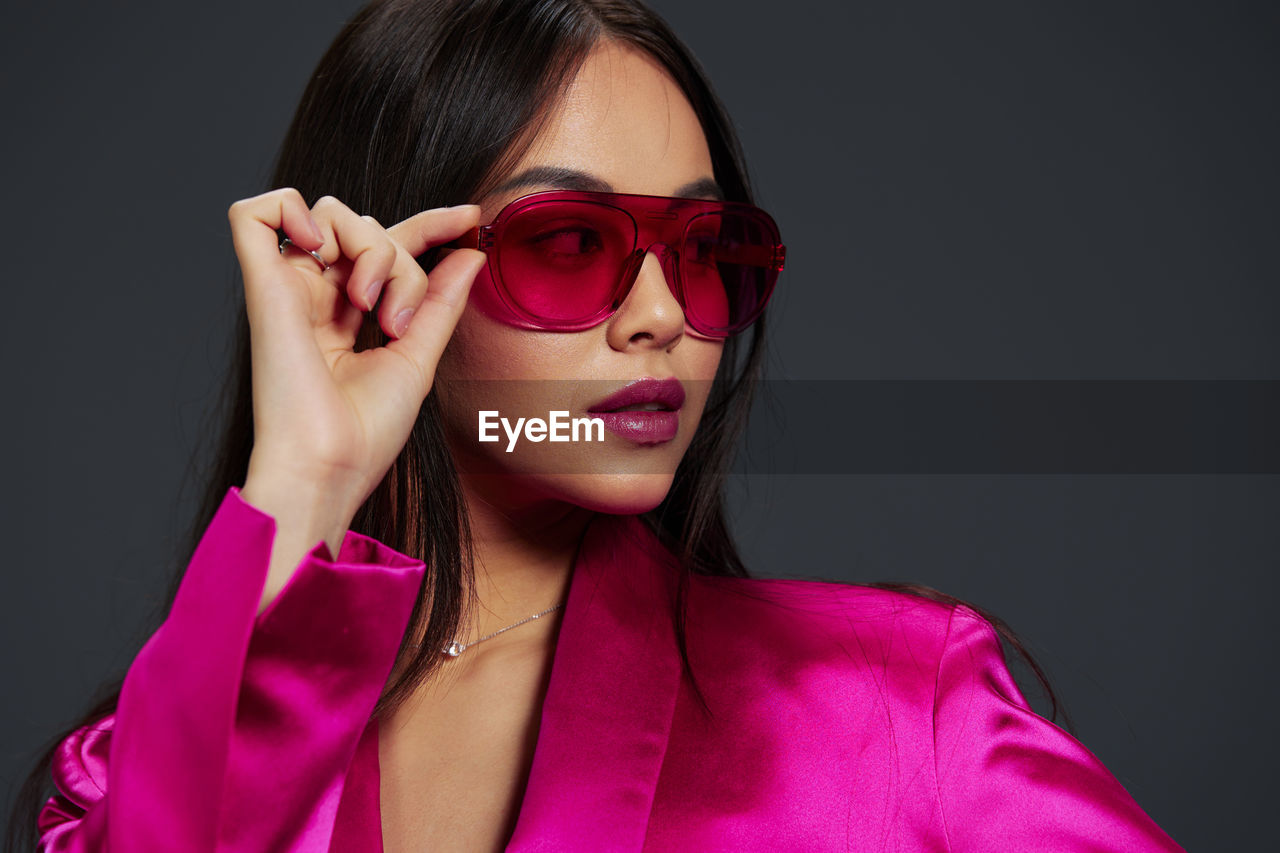 portrait of young woman wearing sunglasses while standing against black background