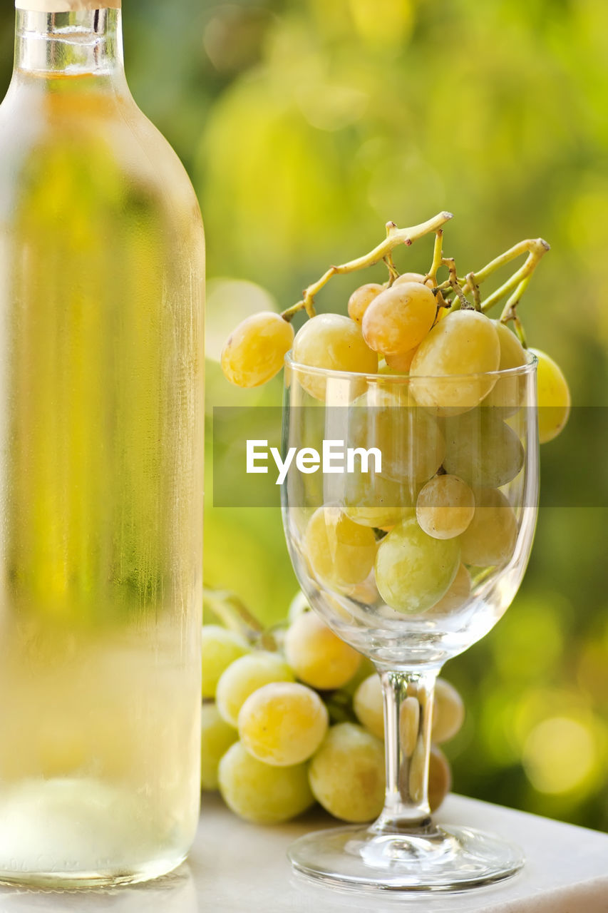 Close-up of wine bottle by grapes filled wineglass on table