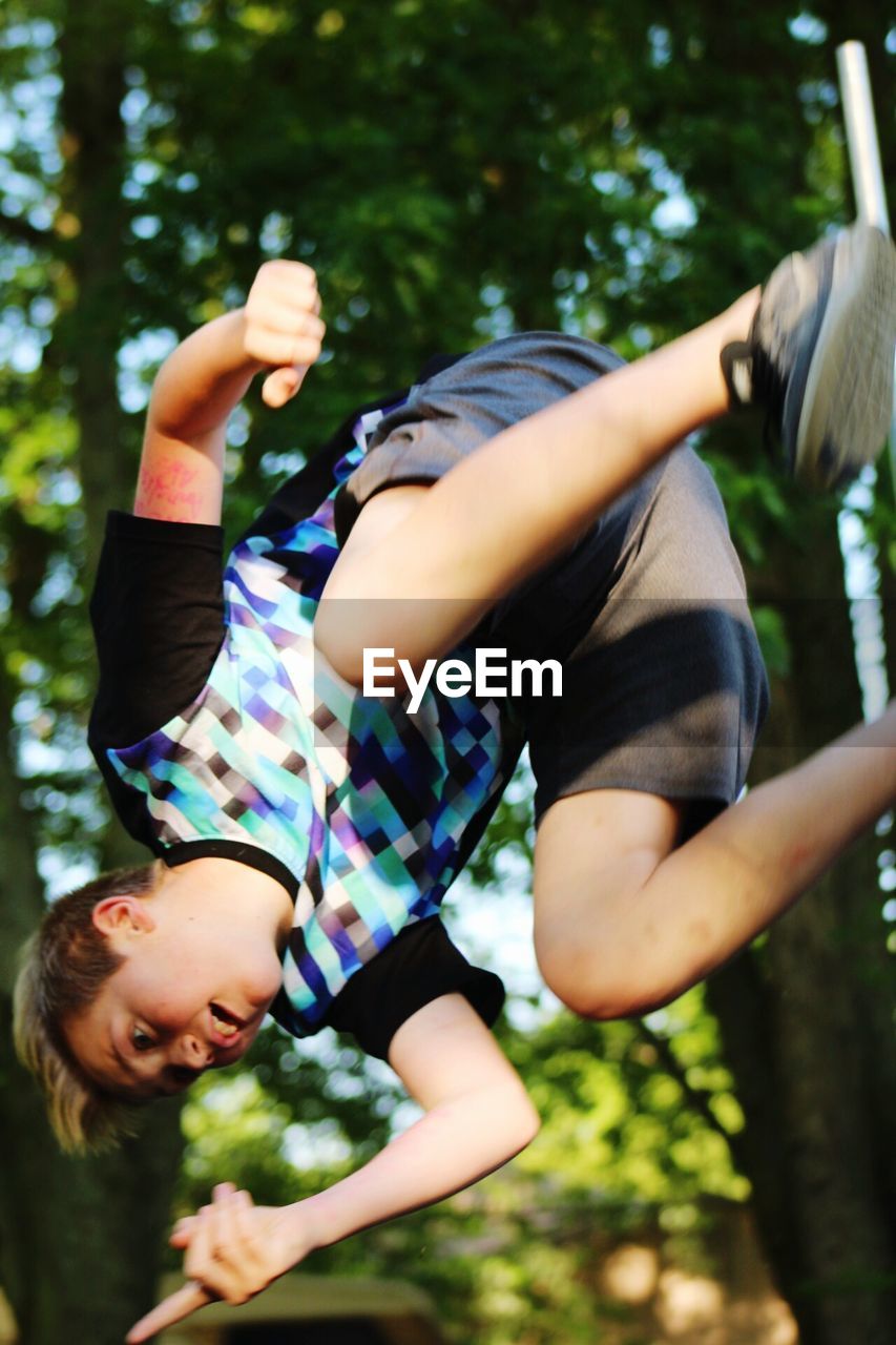 Tilt image of teenage boy jumping against trees