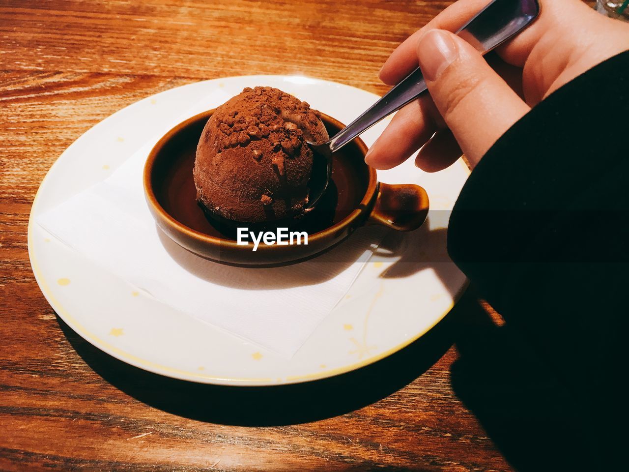 CLOSE-UP OF HAND HOLDING COFFEE CUP WITH CHOCOLATE CAKE