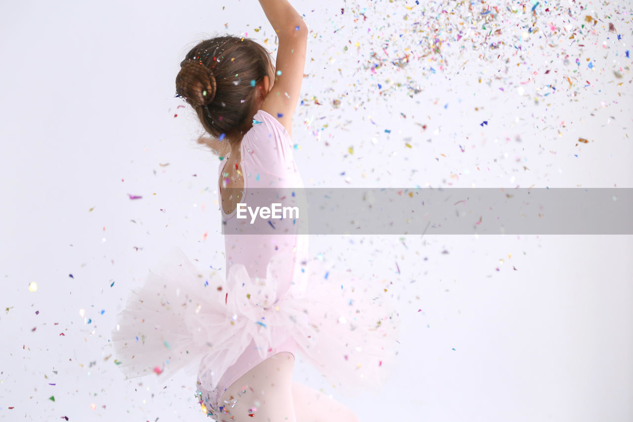 Ballet dancer throwing confetti while standing against white background