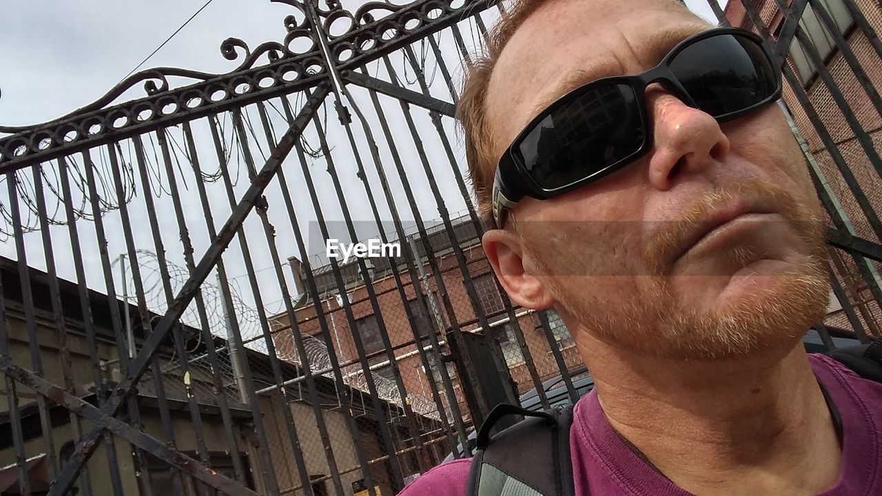 Close-up of mature man wearing sunglasses against closed gate