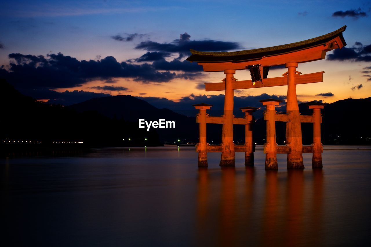 Torii gate in lake against sky during sunset