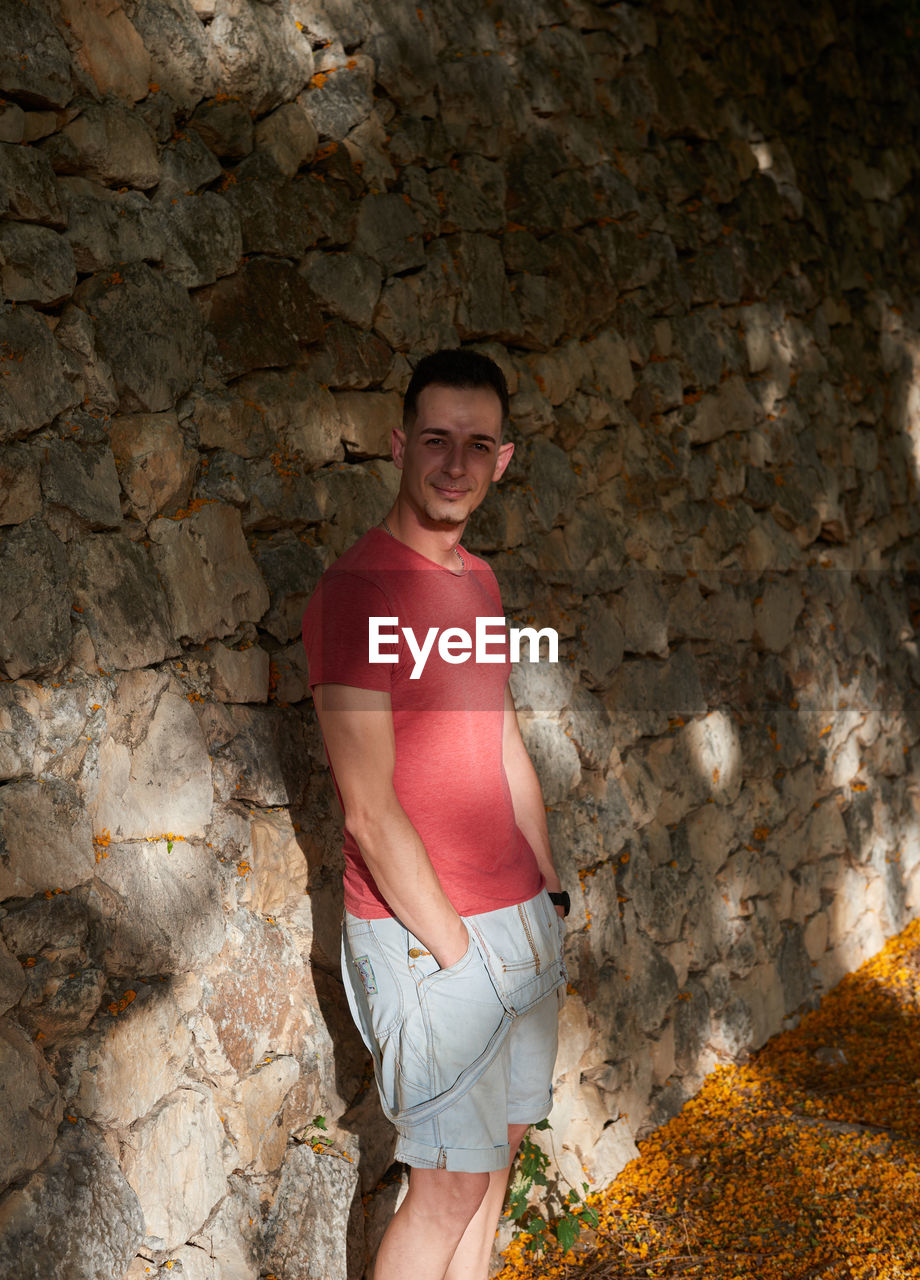 An attractive young man posing on a stone wall.