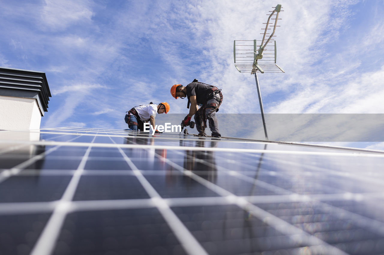 Technician with colleague using drill on solar panel