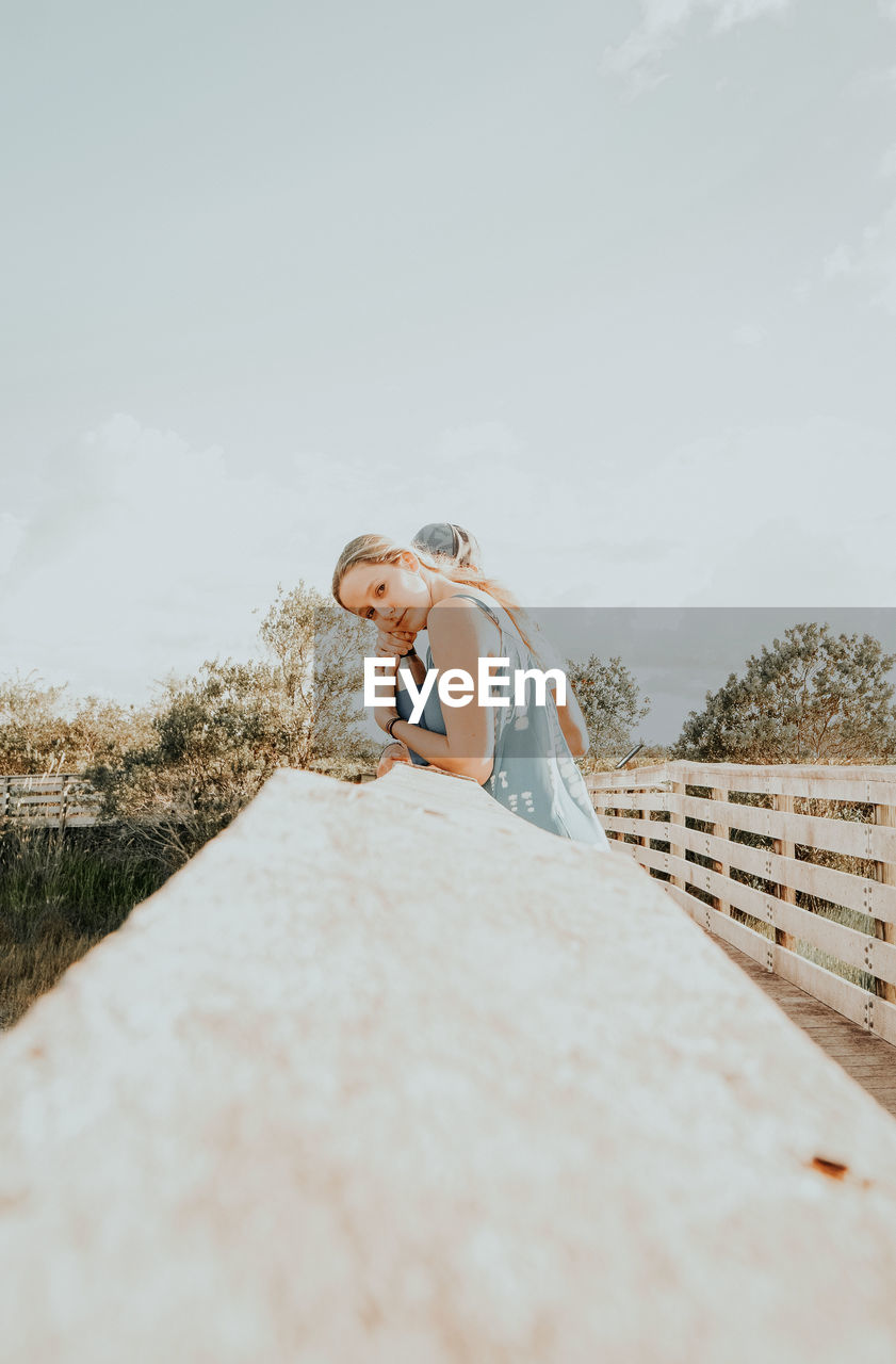 WOMAN STANDING ON WOOD AGAINST SKY