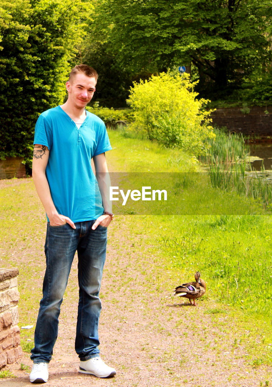 Portrait of young man standing by duck on field