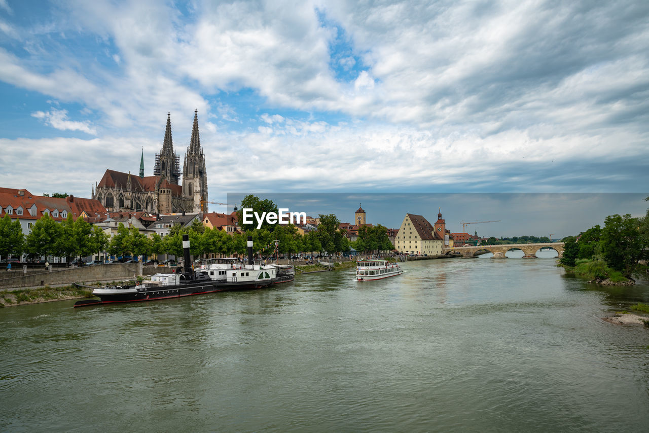 RIVER AMIDST BUILDINGS AGAINST CLOUDY SKY