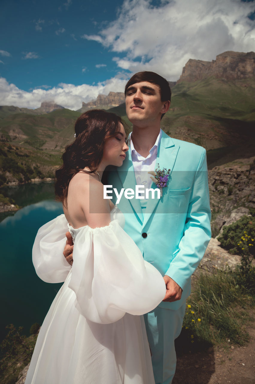 Beautiful wedding couple hugs tenderly against the backdrop of a mountain river and lake, the bride