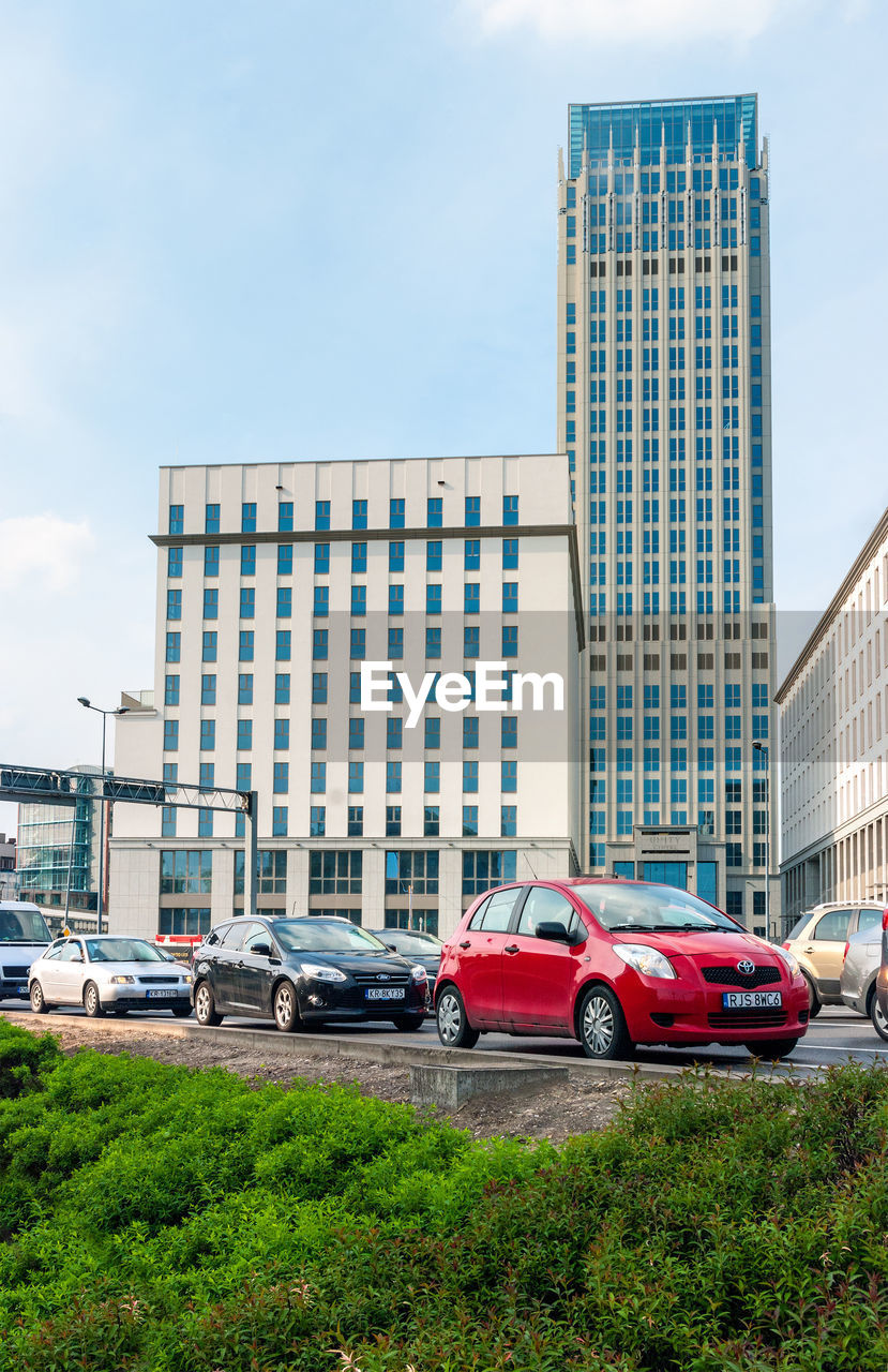 VEHICLES ON ROAD BY BUILDINGS AGAINST SKY