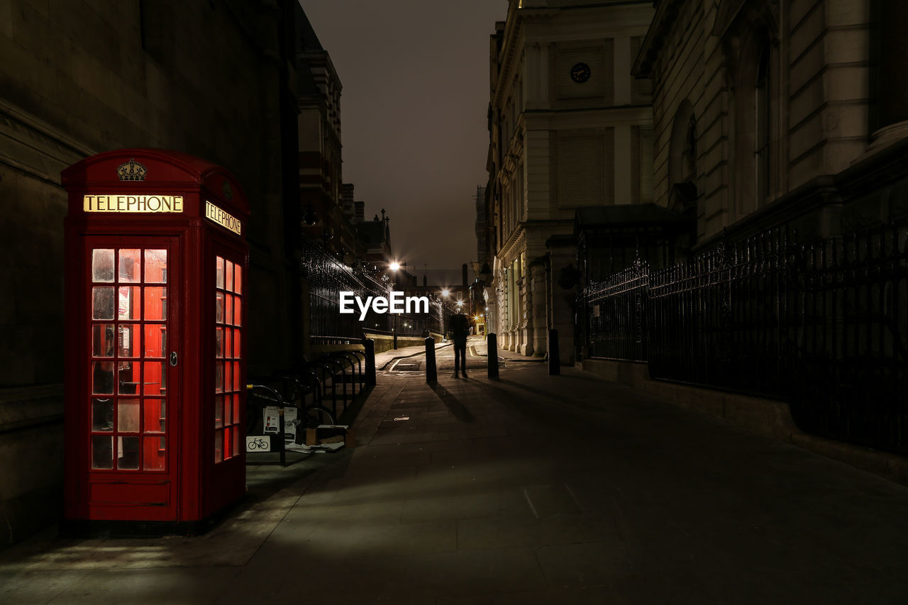 Alley by telephone booth amidst buildings at night