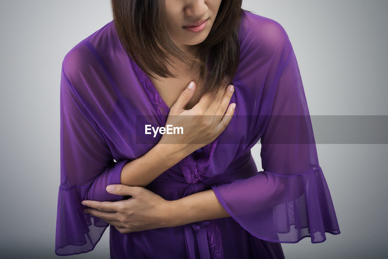 Midsection of woman with chest pain against gray background