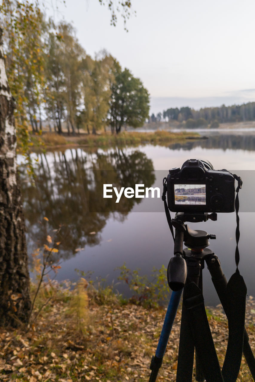 The black digital camera on a tripod shooting early foggy morning landscape at the autumn lake