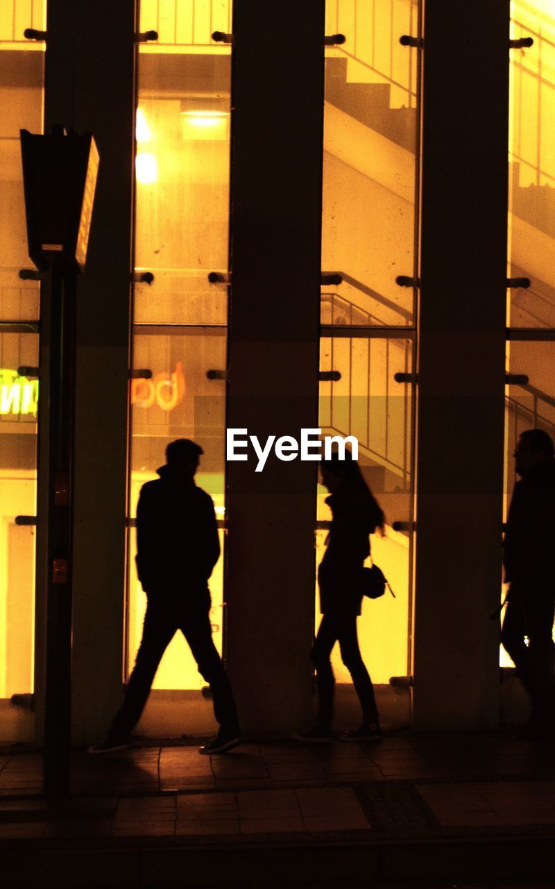 Silhouette people walking in illuminated building