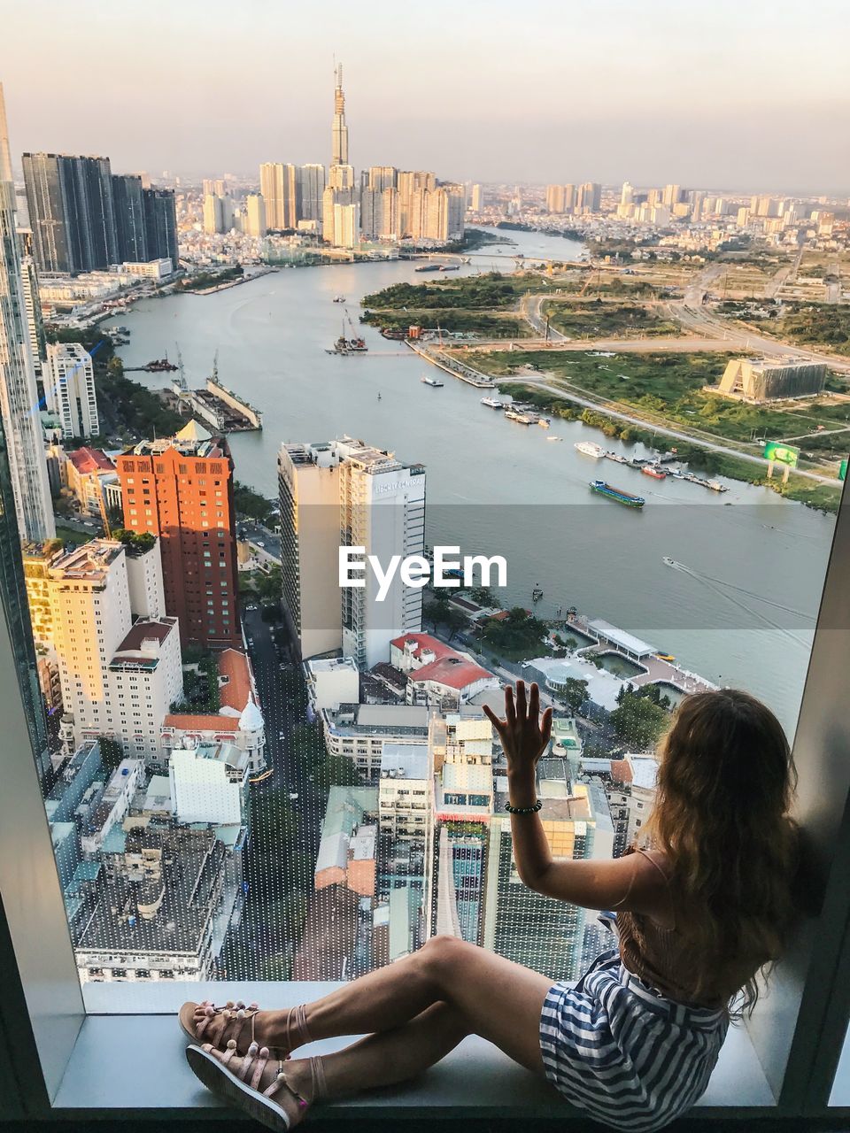 High angle view of mid adult woman looking at cityscape while sitting on window sill
