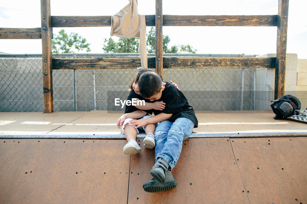 Brother and sister hug while sitting on half pipe