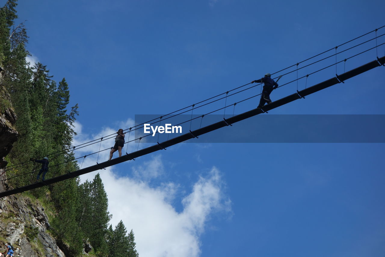 Low angle view of silhouette people walking on footbridge against blue sky