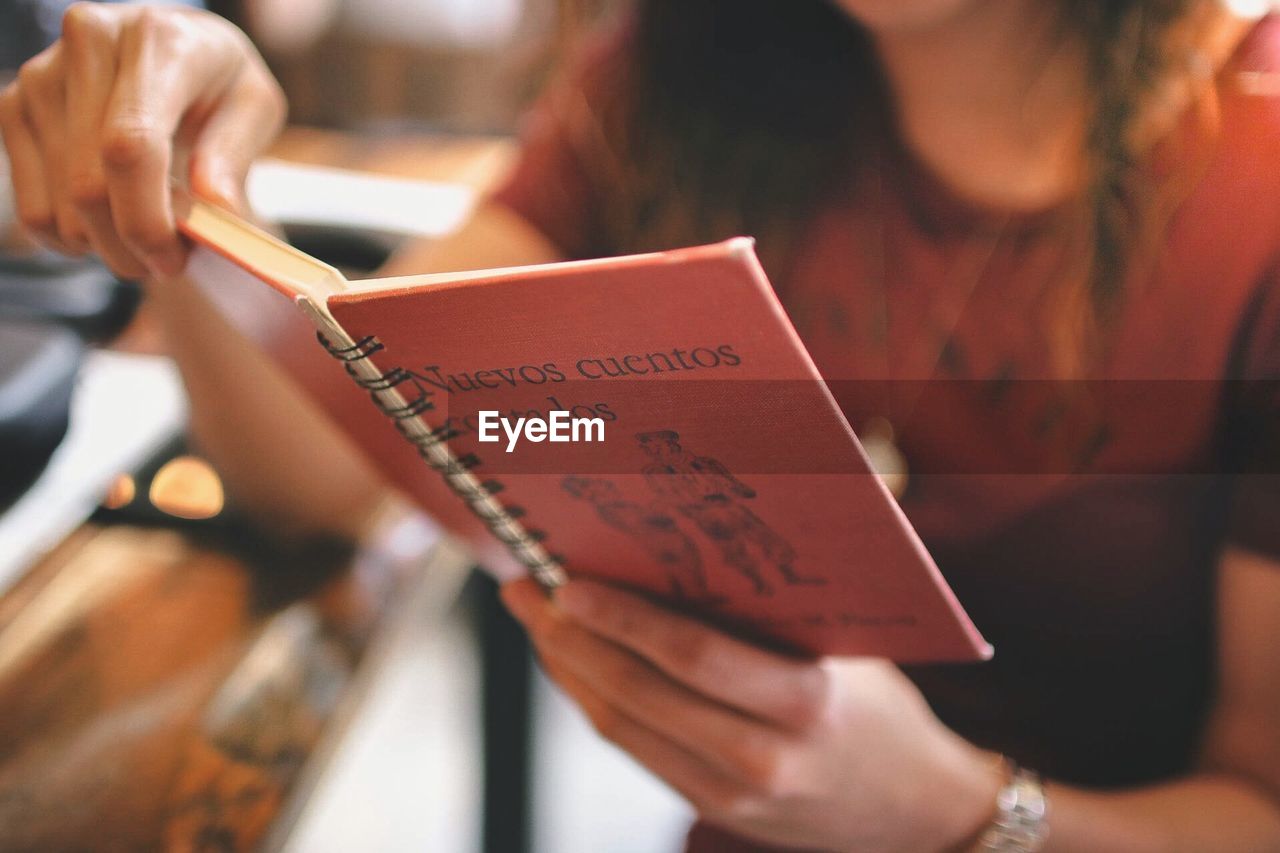 Midsection of woman reading book at cafe