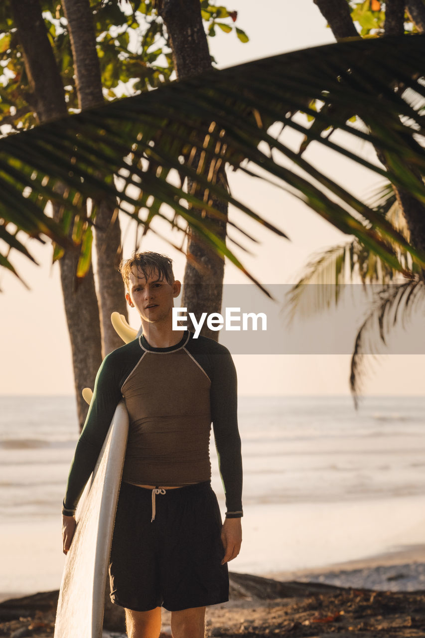 Portrait of confident young man carrying surfboard at beach