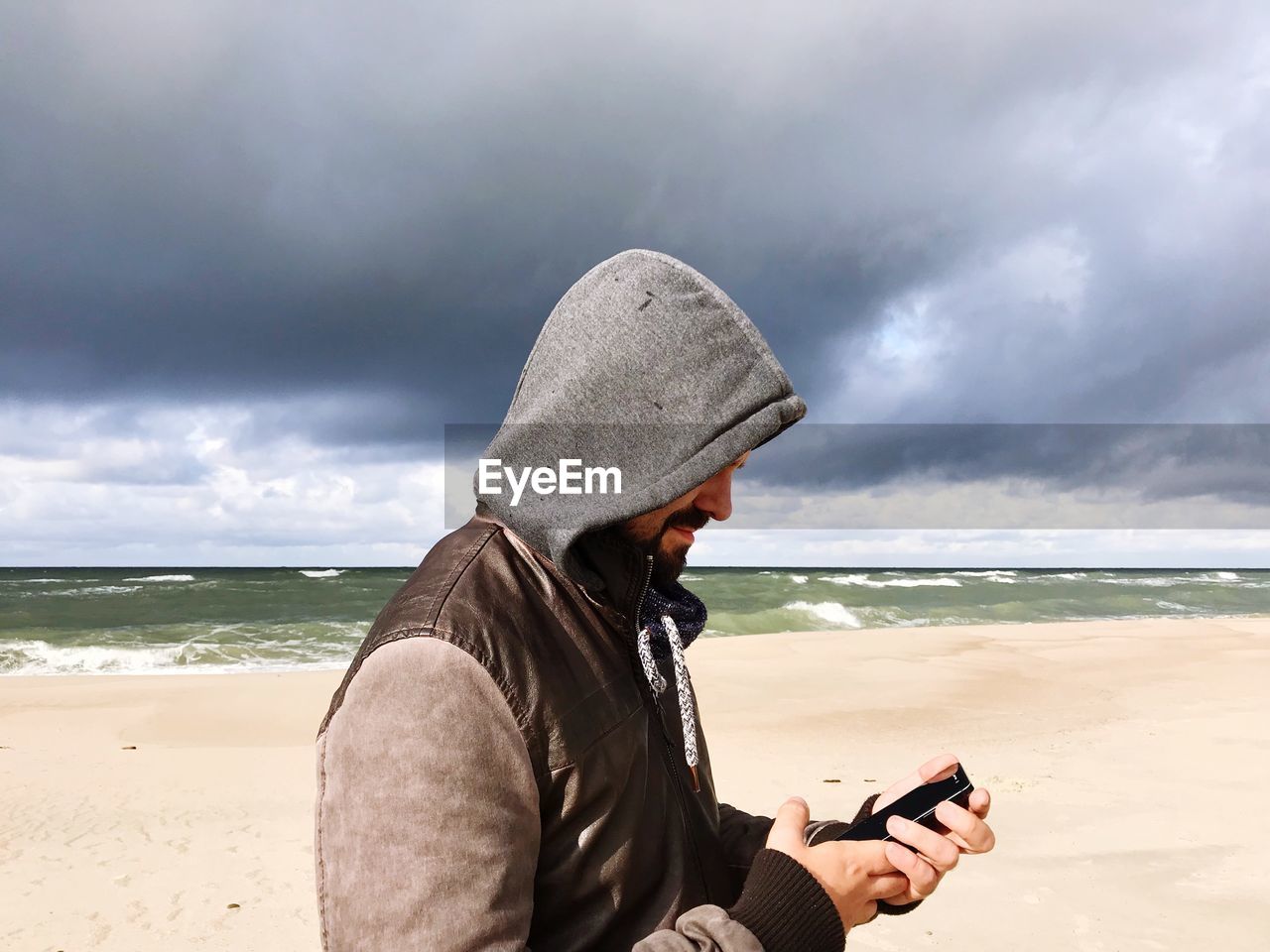 Side view of man using mobile phone at beach against sky