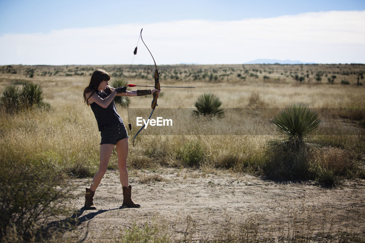 Woman aiming with bow and arrow while standing on field