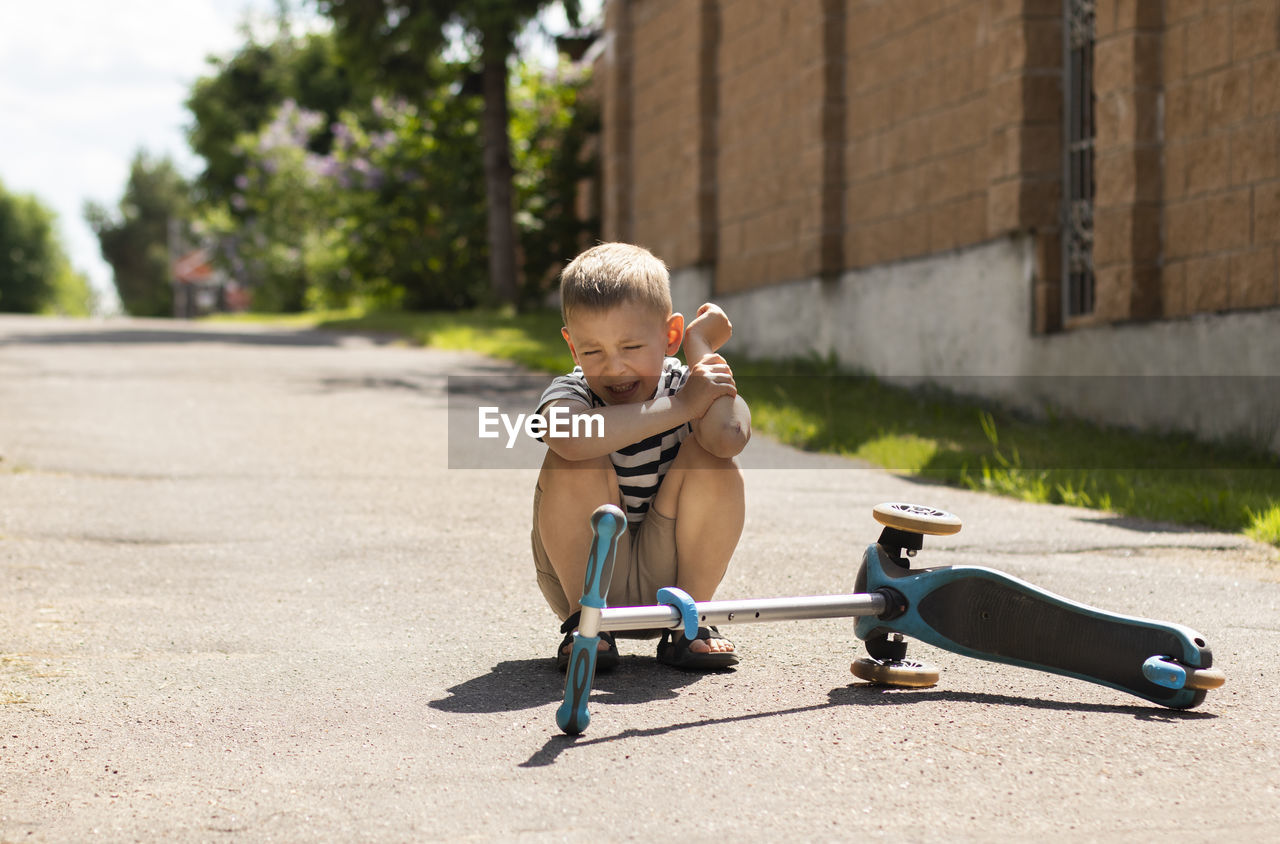 Upset boy crying while falling from push scooter