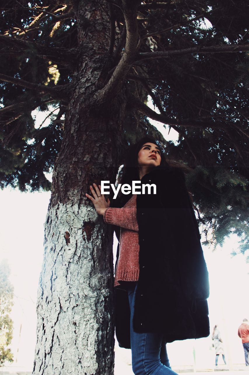 LOW ANGLE VIEW OF WOMAN STANDING BY TREE