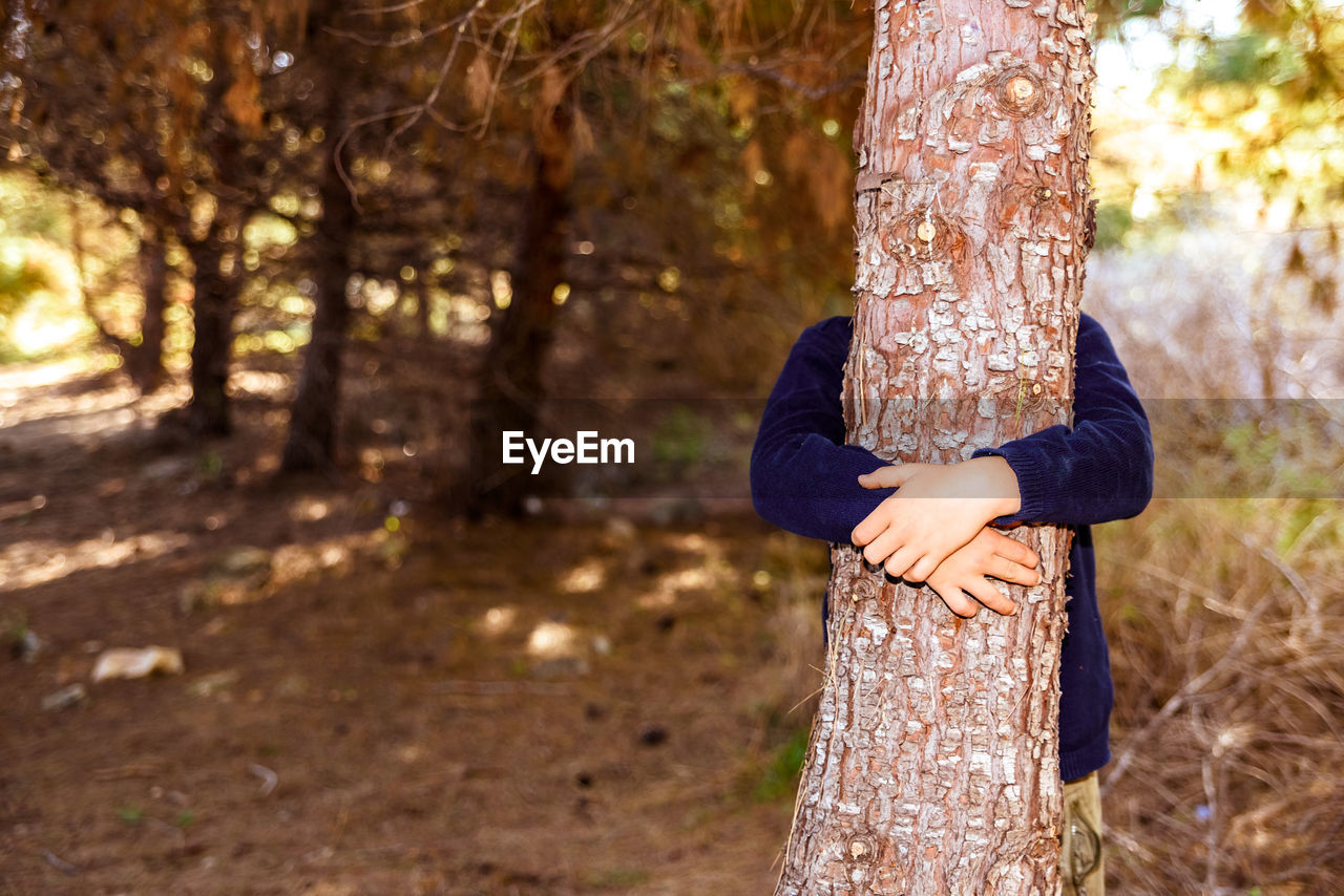 WOMAN STANDING BY TREE TRUNK