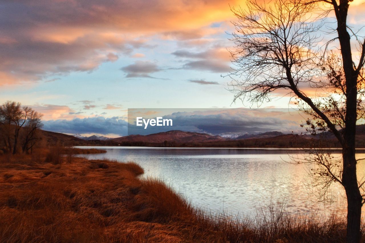 SCENIC VIEW OF LAKE BY MOUNTAINS AGAINST SKY DURING SUNSET