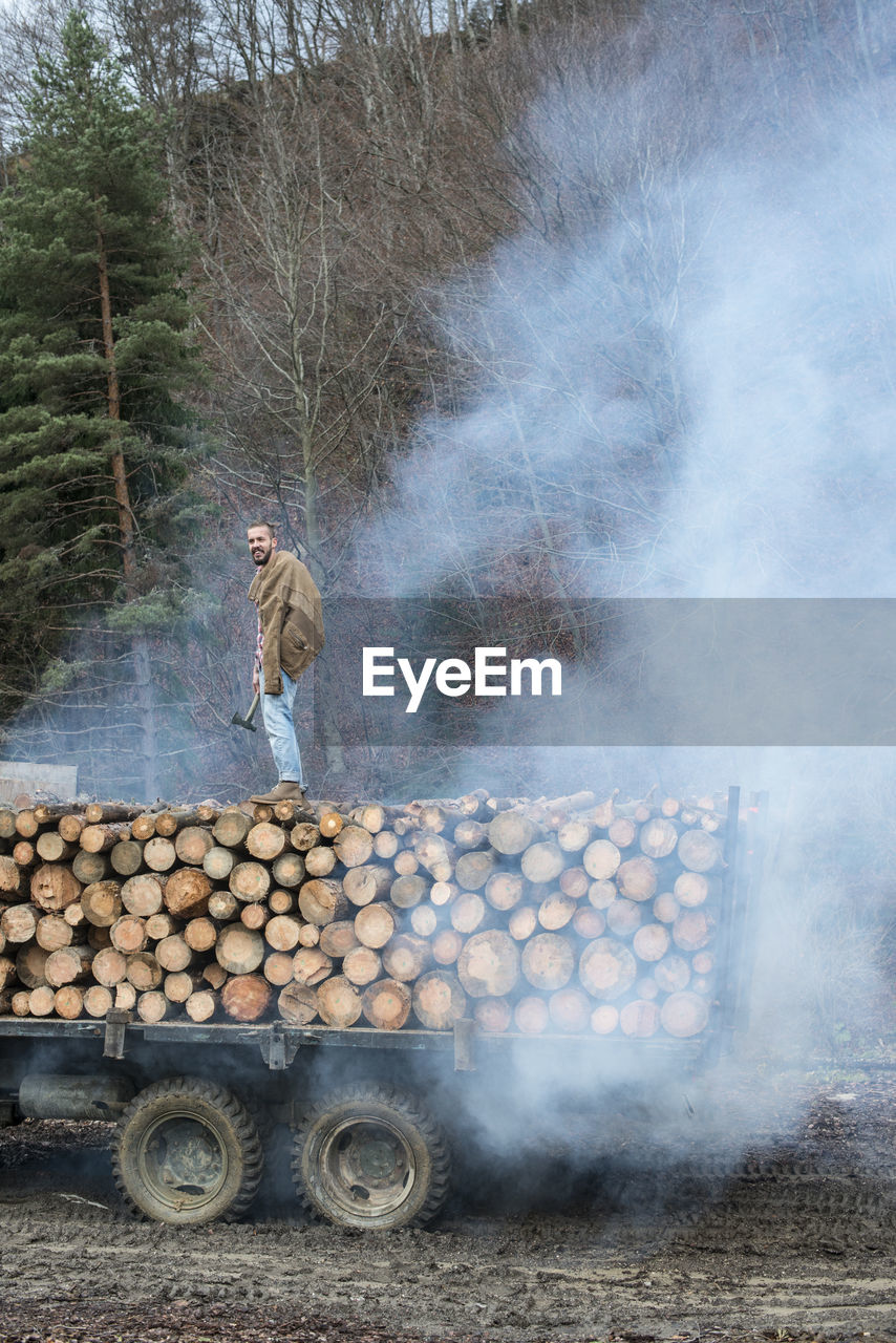 Young man standing on stack of wooden logs on truck