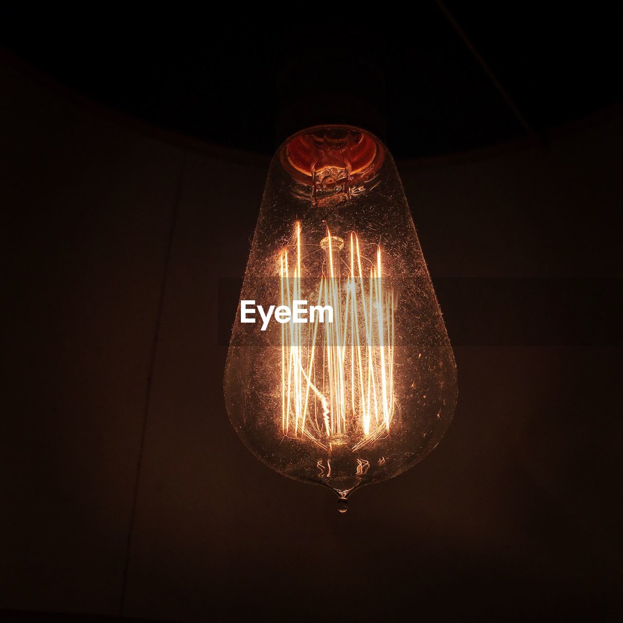LOW ANGLE VIEW OF ILLUMINATED LIGHT BULBS HANGING AGAINST BLACK BACKGROUND